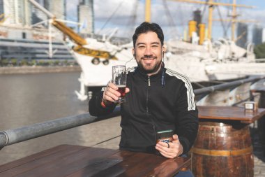 Latin turist bira içiyor, kadeh kaldırıyor ve Puerto Madero, Buenos Aires, Arjantin 'deki bir açık hava barında müzik dinliyor.