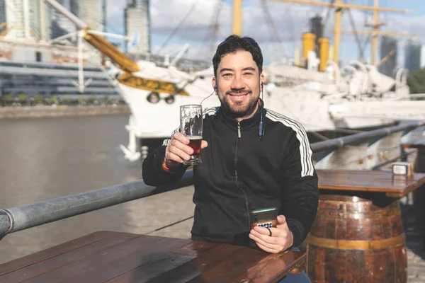 Latin turist bira içiyor, kadeh kaldırıyor ve Puerto Madero, Buenos Aires, Arjantin 'deki bir açık hava barında müzik dinliyor.