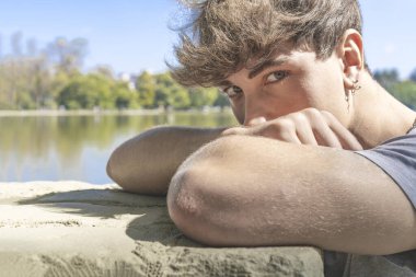 Genç adam kollarının üzerine başını eğip kameraya bakıyor.