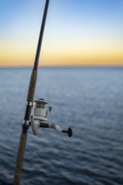 Sahilde dinlenen makaralı olta kamışı, gün batımı zamanı.