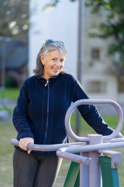 Altmışlı yaşlarındaki bir kadın parkta egzersiz yapıyor. Mutlu yüz ifadesi. Canlılık kavramı.