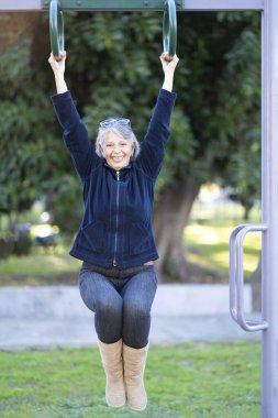 Altmışlı yaşlarındaki bir kadın parkta egzersiz yapıyor. Mutlu yüz ifadesi. Canlılık kavramı.
