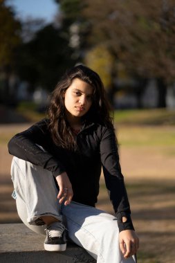 Parkta oturan, yüzünde ciddi bir ifade olan ergen kız.