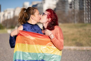 lgbt bayrağına sarılmış transseksüel kadınlar öpüşüyor.