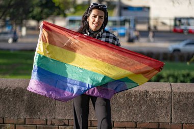 lgbt bayrağı tutan transseksüel kadın kameraya bakıyor.