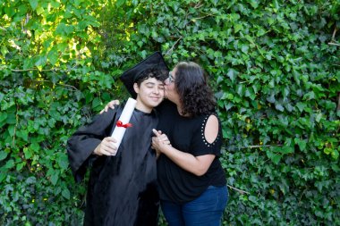 Yakın zamanda mezun olmuş, kep ve cübbe giymiş, diploması elinde, ailesiyle kutlama yapıyor.