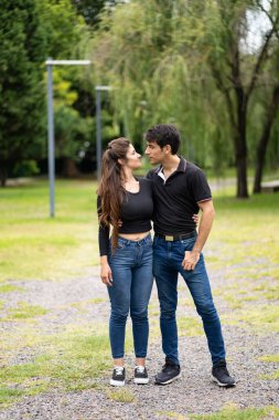 Birbirine aşık genç bir çift parkta kol kola yürüyüp öpüşmek üzere.
