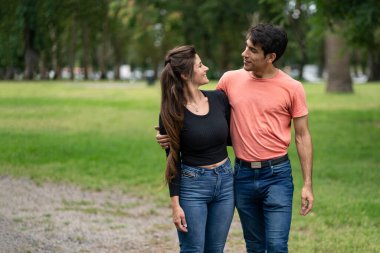 Genç aşık çift parkta kol kola yürüyor.
