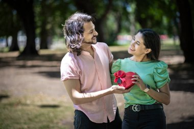 Birbirine aşık çiftler, ellerinde kalp şeklinde bir hediyeyle parkta birbirlerinin gözlerinin içine bakarlar.