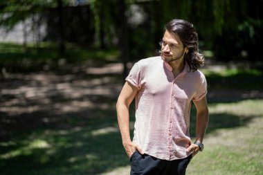 Parktaki genç latin adam, elleri ceplerinde yan tarafa bakıyor.