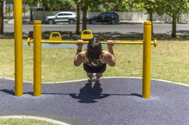 Genç bir adamın parktaki bir barikatın önünde barfiks çekişi.