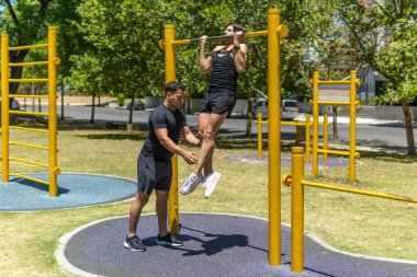 Antrenörü onu düzeltirken parkta barfiks çeken bir adam.