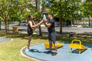 Atletik erkekler esneme egzersizleri yapıyor, parkta antrenman yapmaya hazırlanıyor.