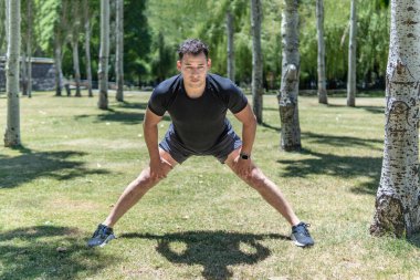 Genç, formda, Latin bir adam şehir parkında antrenman yaptıktan sonra geriniyor.