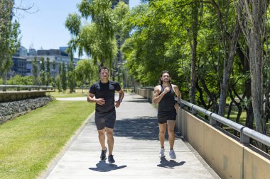 Güneşli bir günde parkta koşan iki genç adam.