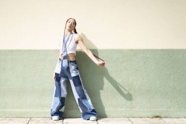 Yamalı kot pantolon ve saç örgüleriyle poz veren kendinden emin bir kadın.