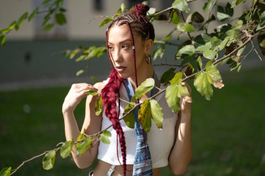 Parktaki yapraklı dalların çerçevelediği düşünceli bir kadının bakışları.