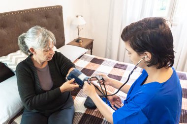 Ev sağlığı uzmanı yaşlı bir kadının yaşam belirtilerini kontrol ediyor.