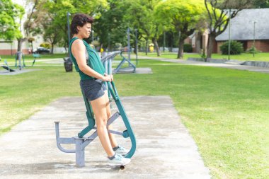 Doğal park ortamında kamusal egzersiz makineleri kullanan bir kadın.