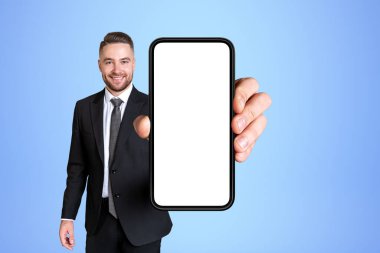 Açık mavi arka planda elinde büyük, boş akıllı telefonu olan mutlu bir iş adamı. İş ağı ve çevrimiçi konferans kavramı