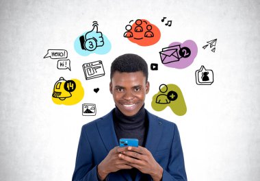 Resmi takım elbiseli gülümseyen Afrikalı Amerikalı işadamı arka planda sosyal medya çizimi olan beton duvarın yanında akıllı telefon tutuyor. İnternet iletişimi, mobil uygulama kavramı