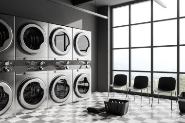 Dark laundry interior with grey washing machines in row, side view waiting corner with chairs on chess tile floor. Panoramic window on countryside. 3D rendering