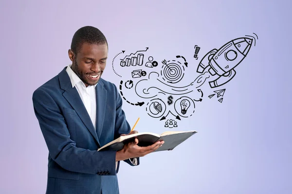 Smiling black businessman writing in notebook, black doodle sketch with start up idea and graphs on lilac background, rocket launch. Concept of project and business plan