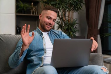 Smiling young businessman waving hand and looking at laptop, online video conference and communication. Concept of online meeting