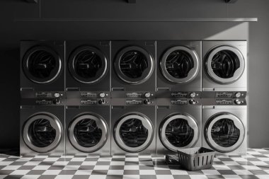 Dark laundry interior with row of grey washing machines and basket, chess tile floor. Modern public laundromat. 3D rendering