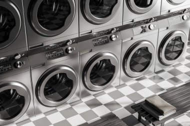 Close up view on dark laundry room interior with ten washing machines, bench, tidy towels, concrete tile floor. Concept of place for washing clothes. 3d rendering