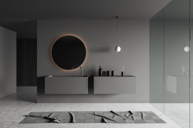 Dark bathroom interior with sink and round mirror with backlight, grey concrete floor with carpet. Glass doors and bathing accessories on deck. 3D rendering