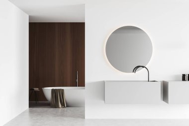 White bathroom interior with sink and round mirror, bathtub with towel in the corner on light concrete floor. Modern hotel washing room. 3D rendering