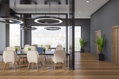 Front view on dark office interior with panoramic windows with town view, tables with armchairs, laptops, lamps and hardwood floor. Concept of place for working process. 3d rendering