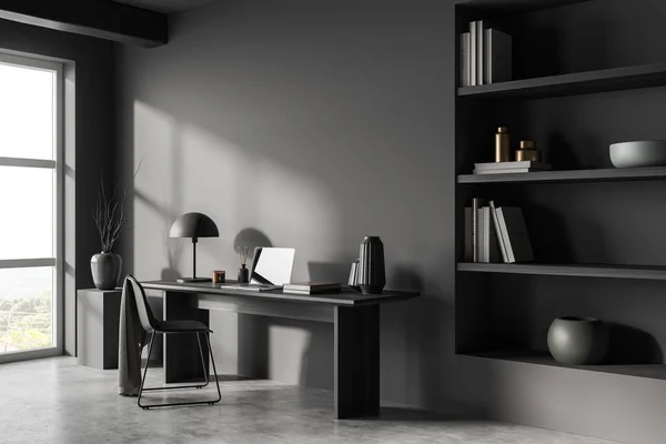 Dark workplace interior with laptop computer on desk, side view, chair on grey concrete floor. Home office with shelf and panoramic window. Mockup copy space. 3D rendering