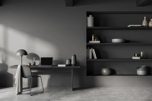 Dark workplace interior with laptop computer on desk, chair on grey concrete floor. Home office with shelf and decoration. Mockup copy space. 3D rendering