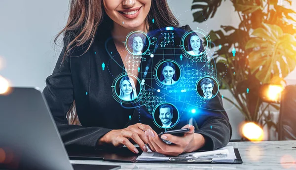 Businesswoman smiling with smartphone in hands, laptop and contract on desk. Earth globe hologram, worldwide social network connection. Concept of distance work and recruitment