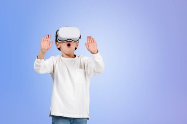 Boy wearing casual wear and vr googles touching metaverse reality with his hands. Blank purple wall. Concept of futuristic technology, virtual reality and progressive kids in business
