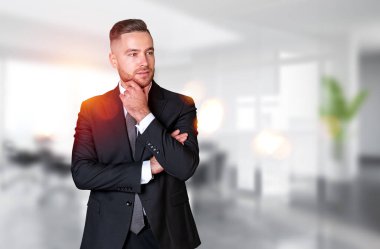Dreaming handsome businessman in formal wear touches his chin with hand at office workplace in background. Concept of ambitious business person, chief, director, knowledge, thinking