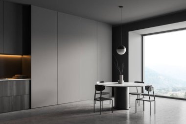 Dark dining room interior with black chairs and round table, side view, panoramic window on countryside, grey concrete floor. Kitchen shelf with appliances. 3D rendering