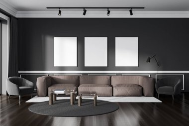 Dark relax hall interior with sofa and armchair, coffee table on carpet, hardwood floor. Chill space and three mockup posters in row on dark wall. 3D rendering