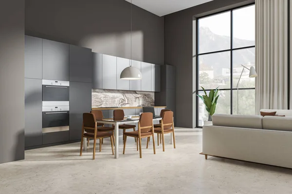 Dark kitchen interior with dining area with chairs on light concrete floor, side view. Chill zone with sofa in hotel studio, panoramic window on countryside. 3D rendering