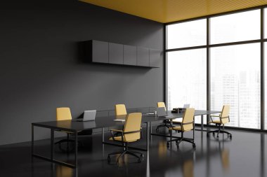 Dark office interior with shared table and laptop, side view black concrete floor. Meeting corner with panoramic window on skyscrapers. 3D rendering