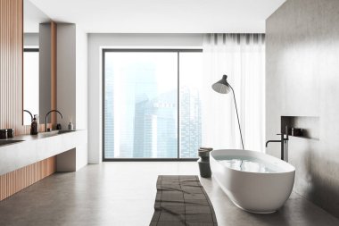White bathroom interior with sink and bathtub, accessories and foot towel on grey concrete floor. Panoramic window on Singapore skyscrapers. 3D rendering