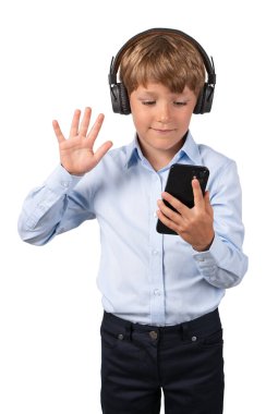 Smiling child boy in headphones, waving hand and looking at smartphone, isolated over white background. Concept of video conference call and online education