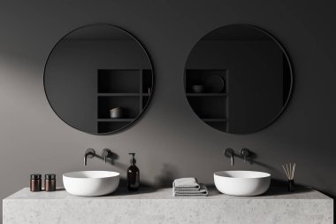 Dark bathroom interior with two sink and round mirror, grey concrete deck with bathing accessories, reed diffuser and bath gel. 3D rendering