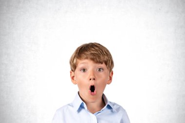 Portrait of surprised little boy over concrete wall background. Concept of emotions, surprise and education. Thinking and planning, good idea