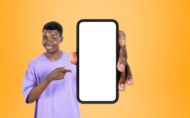 Elinde akıllı telefonu işaret eden gülümseyen siyah adam, sarı arka plan. Mobil uygulama ve web sitesi kavramı. Boşluk görüntüsünü kopyala