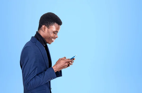 Young black businessman profile with a happy smile browse smartphone, light blue background. Concept of online communication and messenger. Copy space.