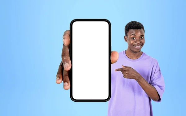青い背景にスマートフォンを指差しているアフリカ人の笑顔の男の指 ソーシャルメディアとウェブサイトの概念 コピースペースの表示をモックする — ストック写真