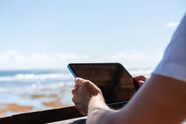 Genç adam elinde tablet, plajın bulanık arkaplanı ve boş bir kopya uzay gökyüzü tutuyor. Çevrimiçi bağlantı ve internet taraması. Seyahat ve turizm kavramı